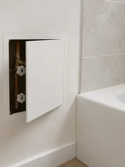 A white access panel set into a tiled wall beside a bathtub