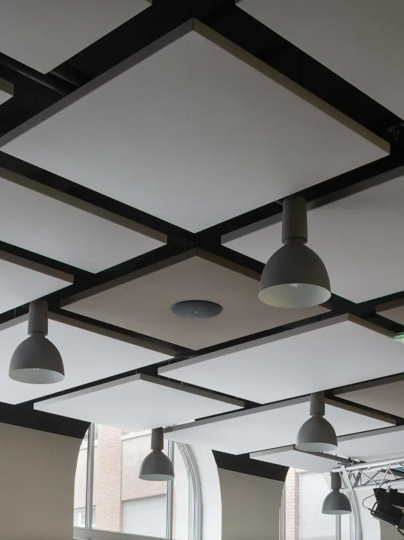 White acoustic ceiling panels suspended in a black grid with integrated lighting