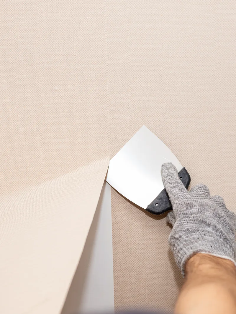 A worker lifting a sheet of wallcovering away from the wall with a knife
