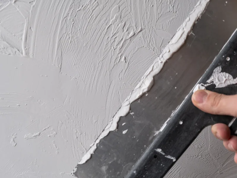 White compound spread over a grey wall with the edge of a broad knife
