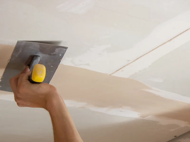 A trowel drawing joint compound along the join between wall and ceiling
