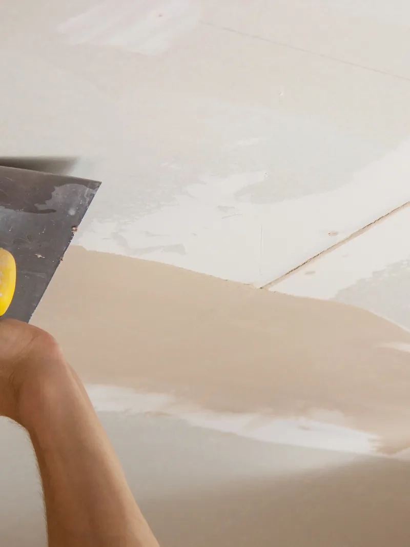 A trowel drawing joint compound along the join between wall and ceiling