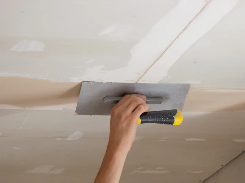 A hand flattening compound across an overhead ceiling seam