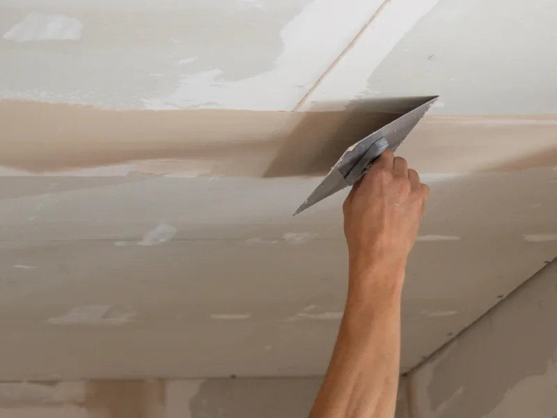 A trowel worked along a ceiling seam from below at arm's length