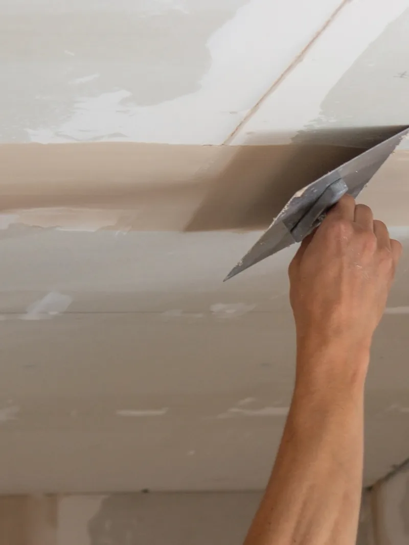 A trowel worked along a ceiling seam from below at arm's length