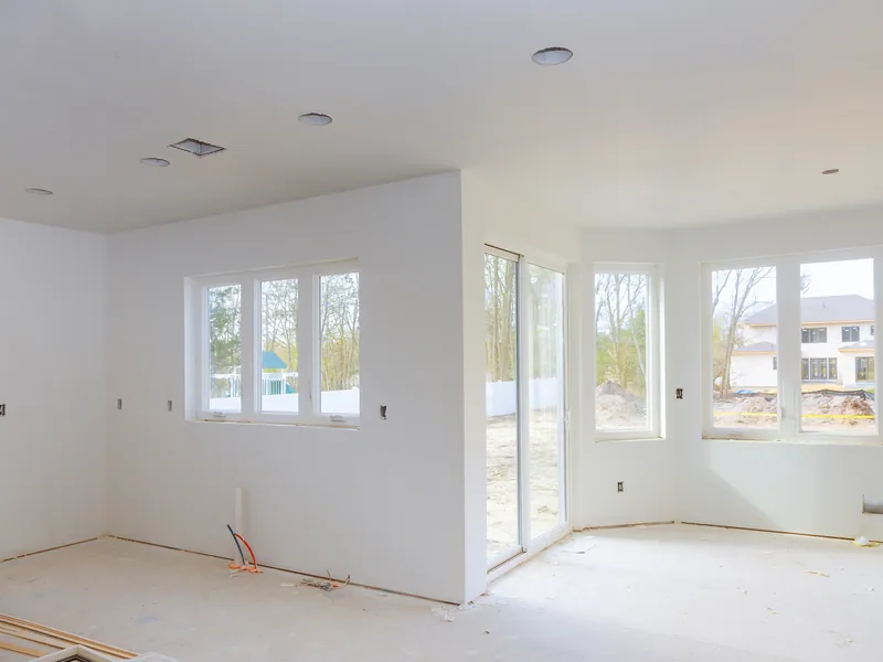 An empty white room with finished walls and daylight from three windows