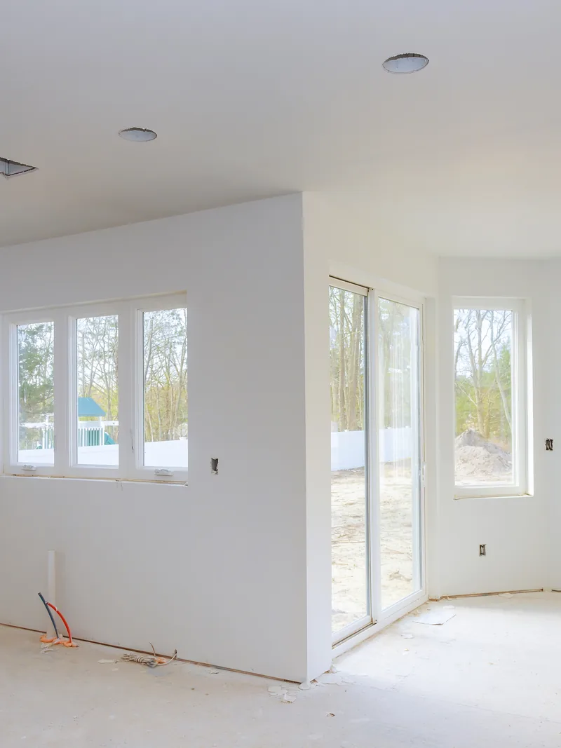 An empty white room with finished walls and daylight from three windows
