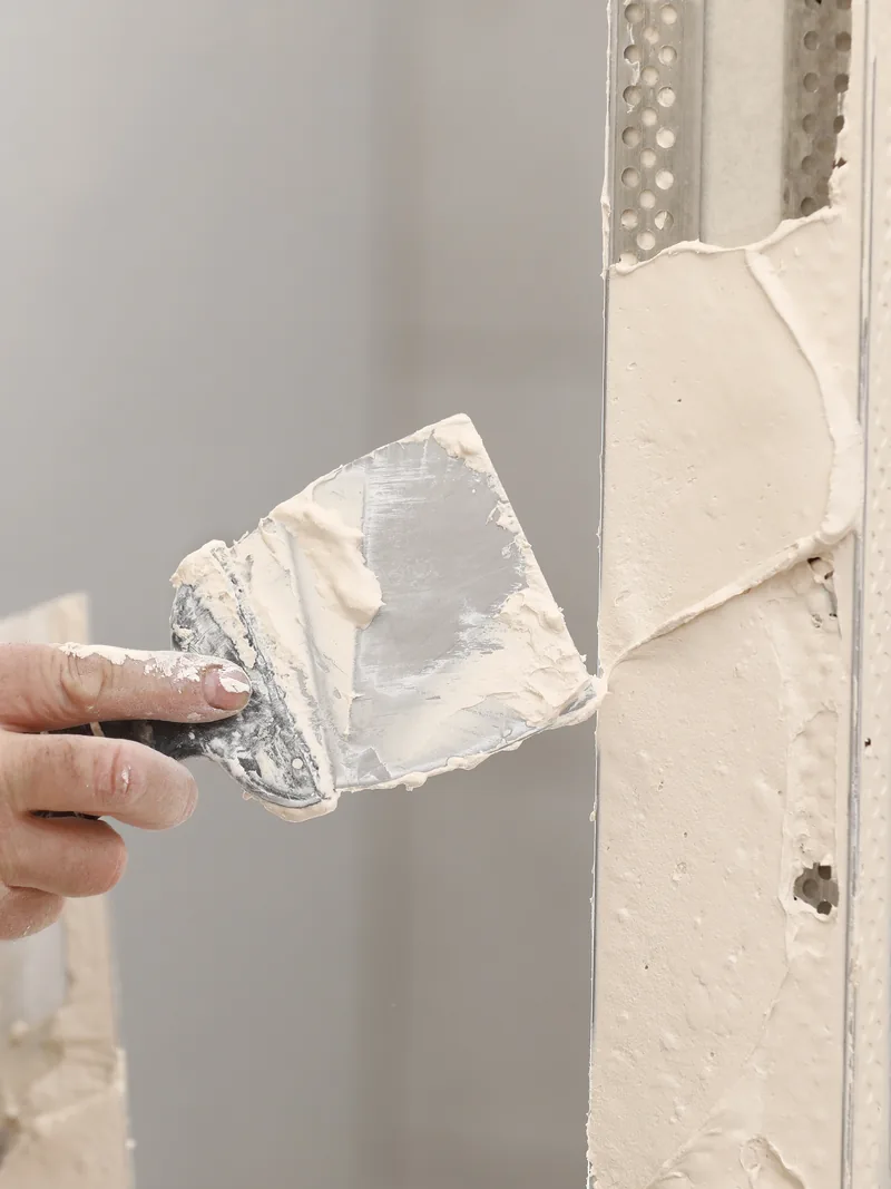A trowel loaded with plaster pressed into a patch at the edge of a wall