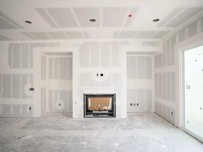 A large taped and mudded living room with a fireplace opening framed in