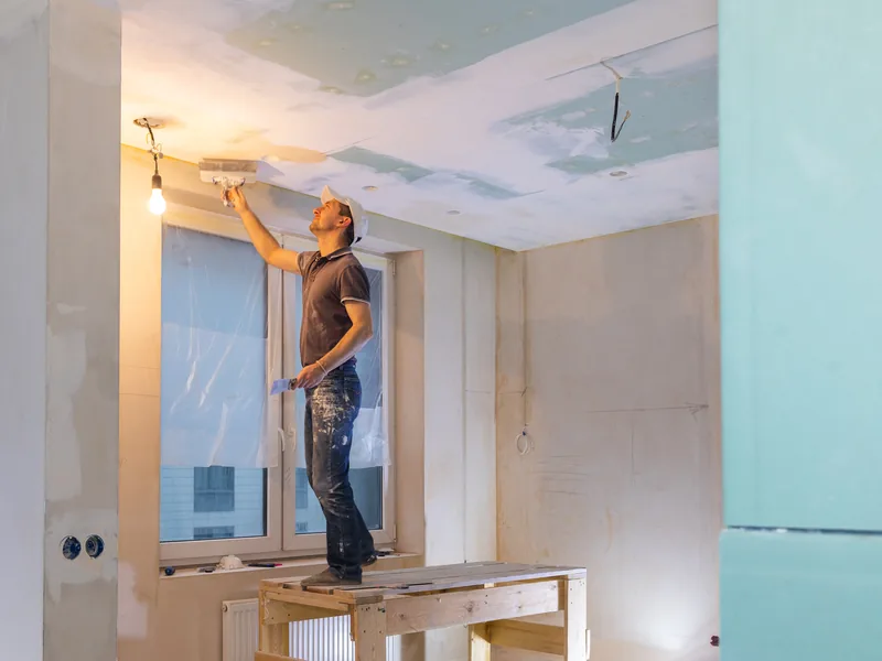 A worker standing on a box to run compound along the top of a wall