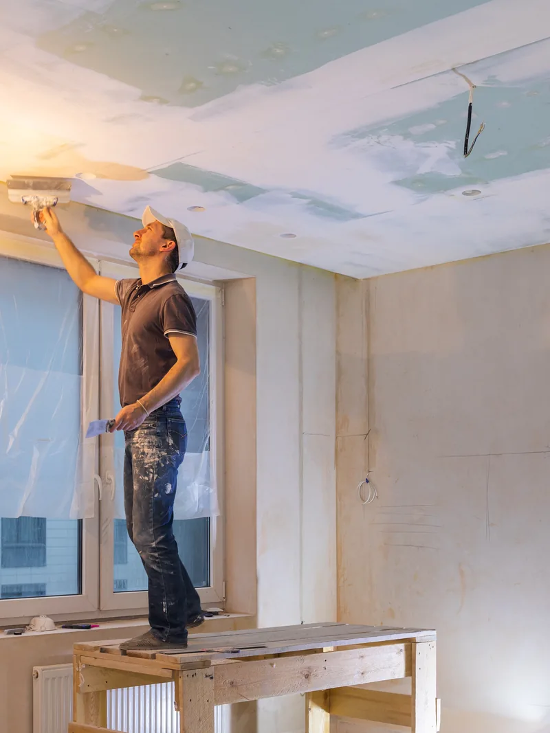A worker standing on a box to run compound along the top of a wall