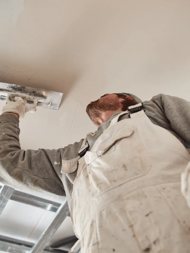 A worker reaching overhead with a knife at a suspended ceiling frame