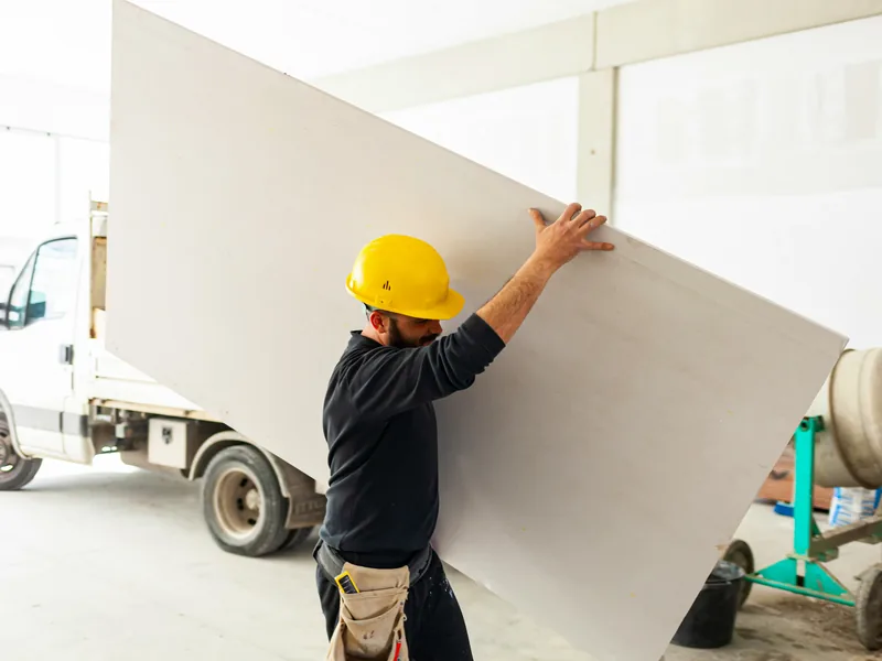 A worker lifting a single panel down beside a flatbed truck
