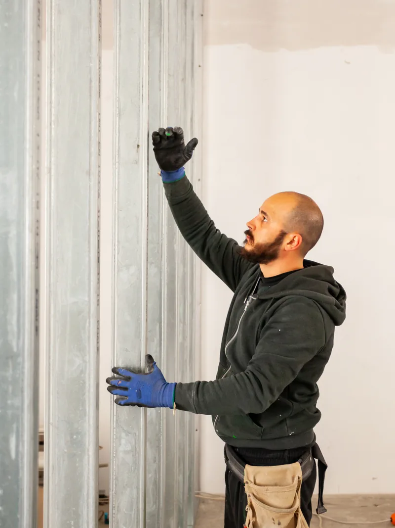 A worker setting a steel stud into a track inside a part-framed opening