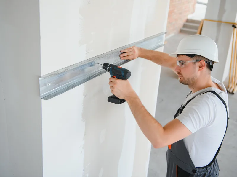 A worker drilling a steel track into place against a boarded wall