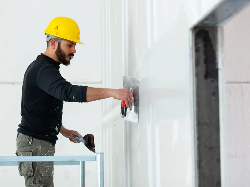 A worker finishing the face of a wall next to a squared structural column