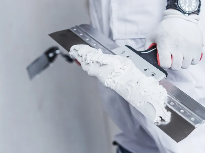 A broad knife held up loaded with a ridge of joint compound