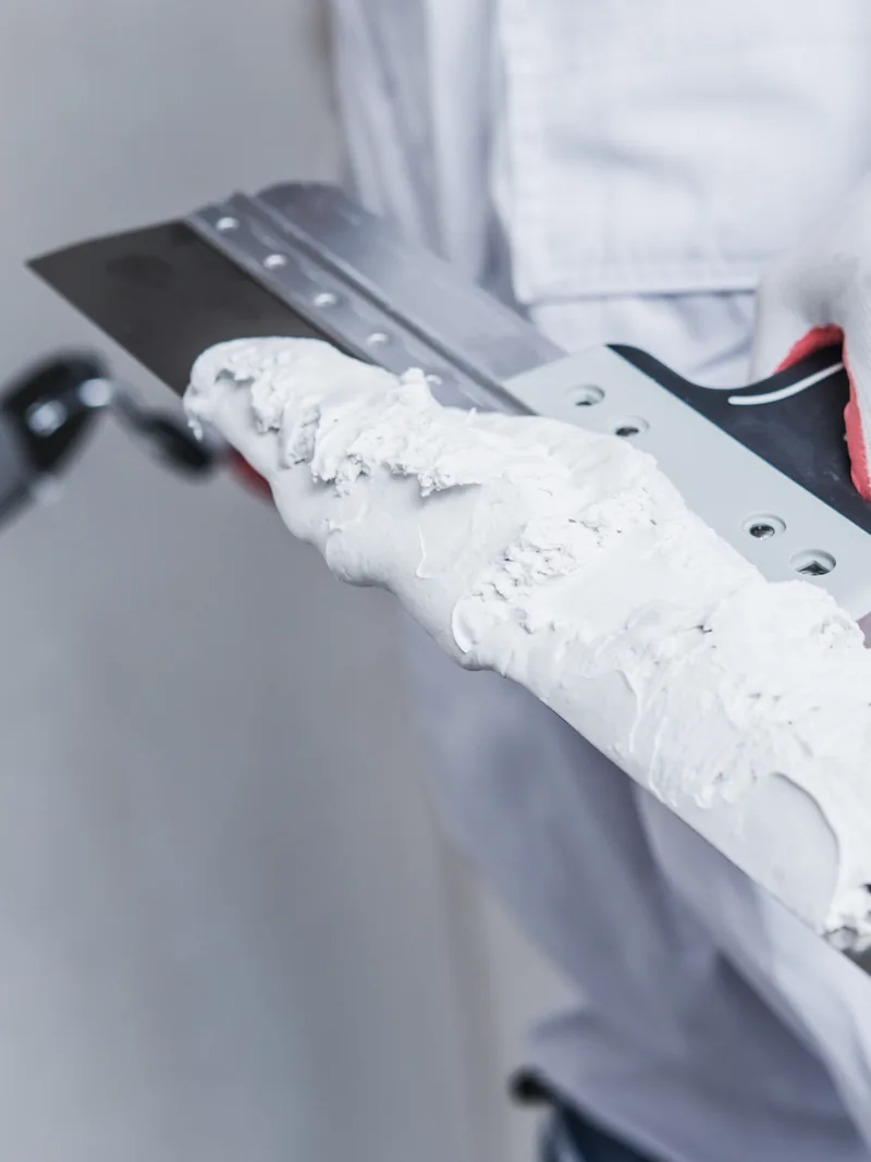A broad knife held up loaded with a ridge of joint compound