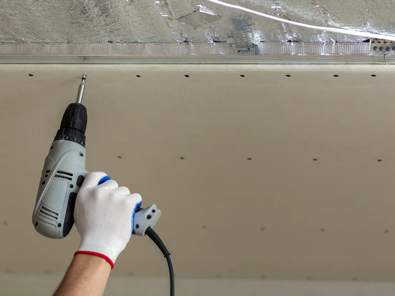 A cordless drill setting a screw into a ceiling panel