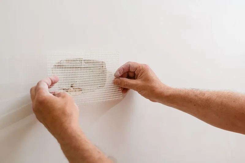 Hands pressing a self-adhesive mesh patch over a small hole in a wall