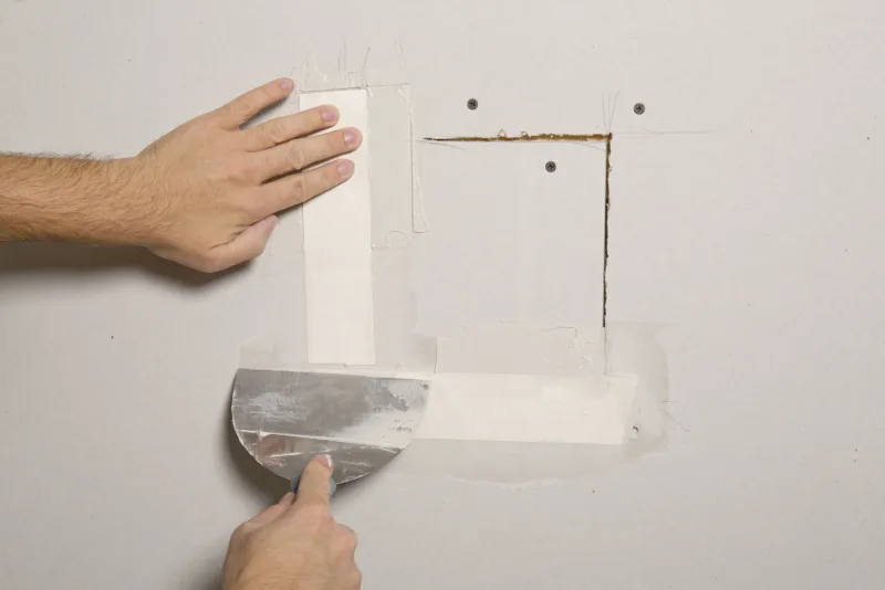 Paper tape bedded in joint compound over a square drywall patch