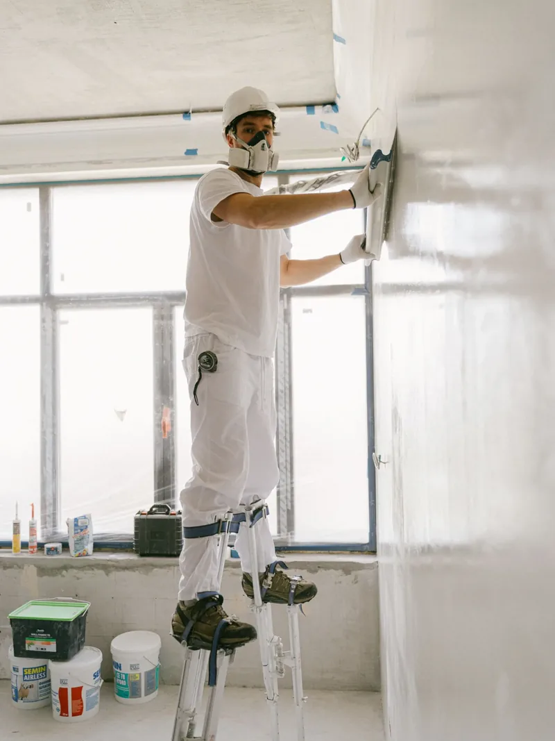 Finisher on drywall stilts applying a Level 5 skim coat