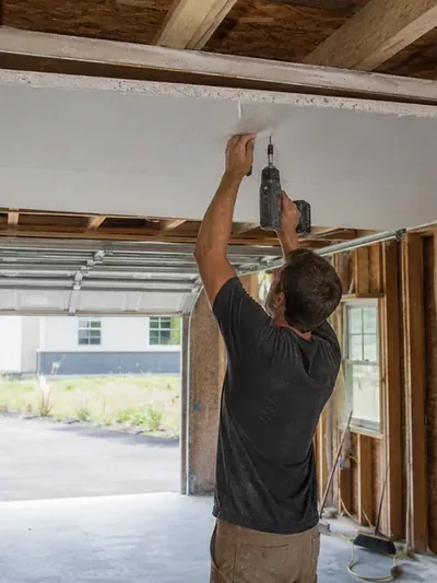 A worker screwing board to the ceiling of an open garage