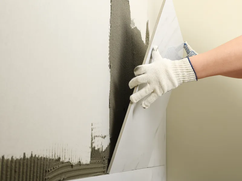 Gloved hands pressing a panel onto a combed bed of adhesive