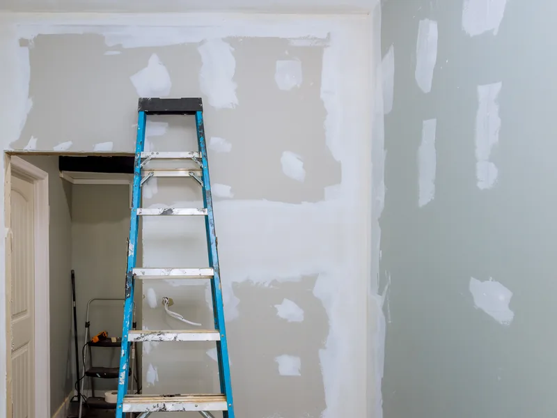 A stepladder standing in a room whose walls are spotted with filled patches