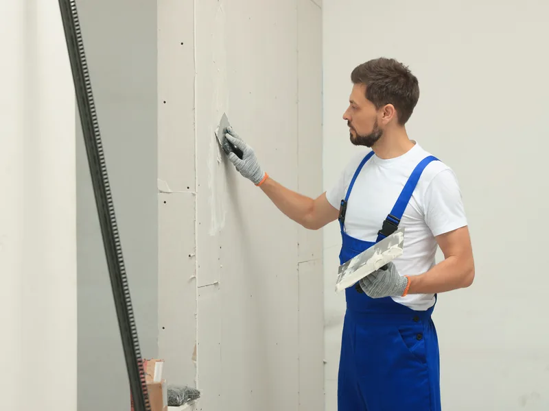 A worker flattening a wall with a sanding block held in both hands