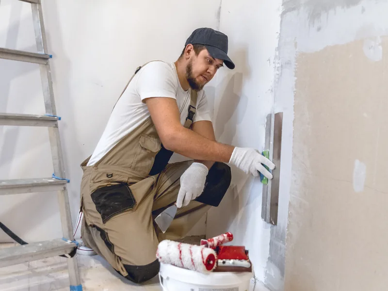 A worker crouching to fill a patch low down on a wall