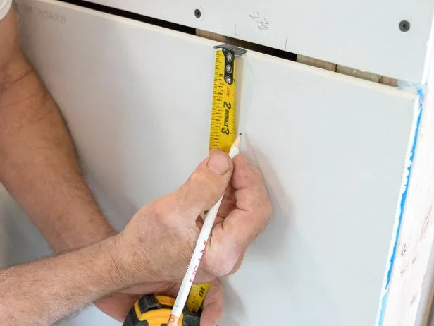 A tape measure held across a drywall panel before it is cut