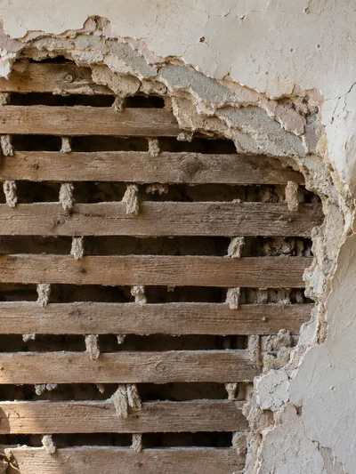 Plaster broken away from a wall to expose the wood lath behind it