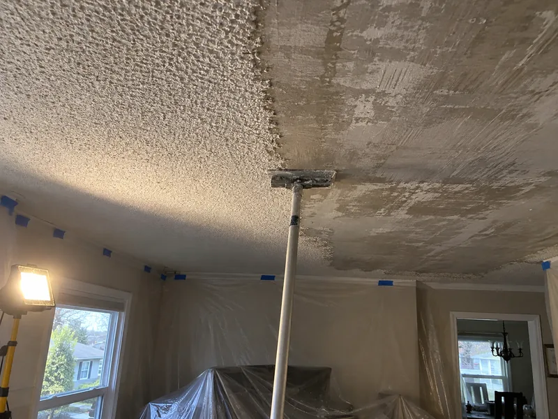 A popcorn ceiling half removed with the pole scraper still against it