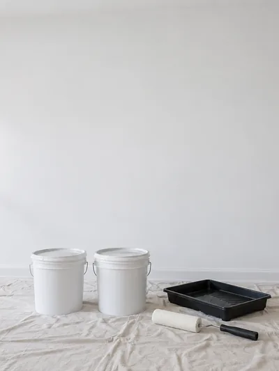 A primed wall with unopened paint tubs and a tray set out below it