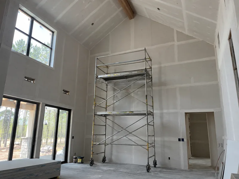 Rolling scaffold staging against a boarded two-storey wall under a ceiling sloping away to a ridge