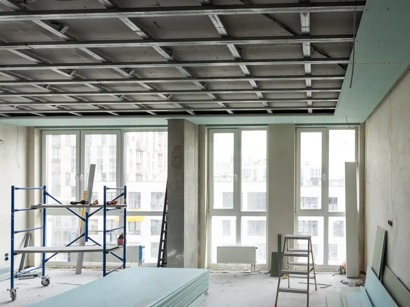 A commercial room with an open suspended ceiling grid and a scaffold tower