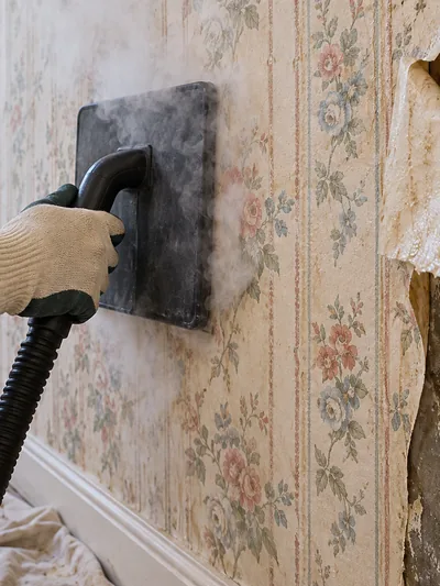 A steamer plate held to a papered wall as the paper peels away beside it