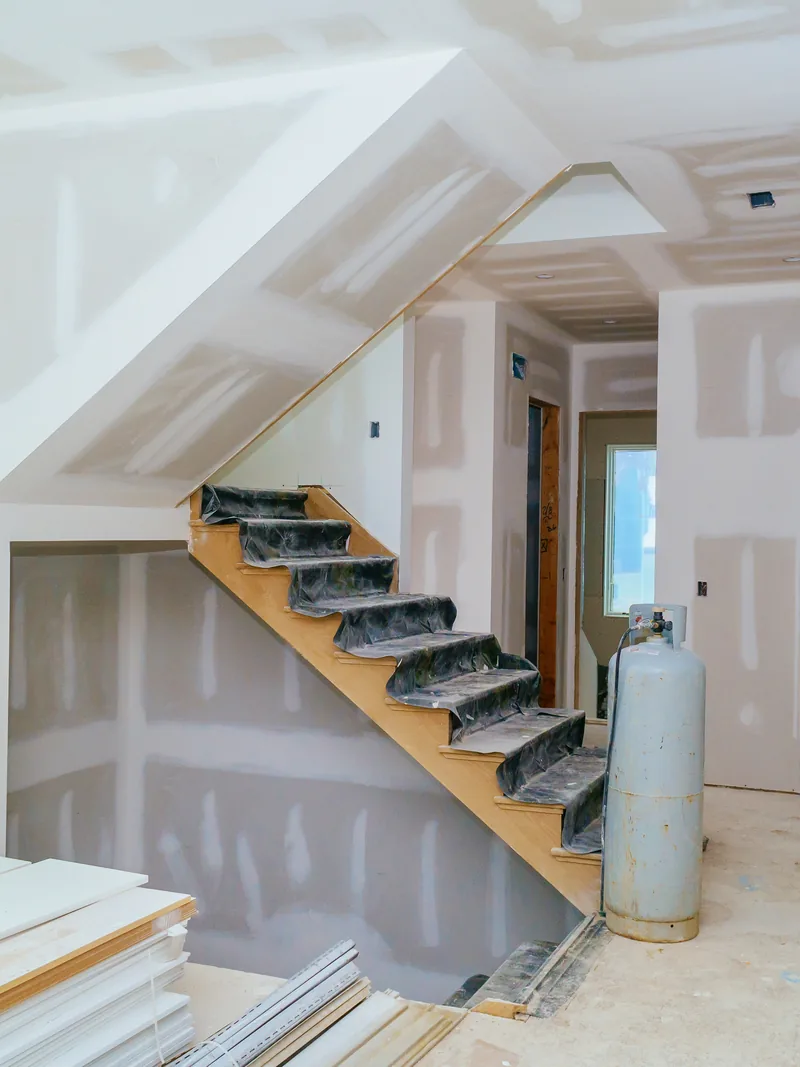 A boarded stairwell with panels and tools stacked at the foot of the stairs
