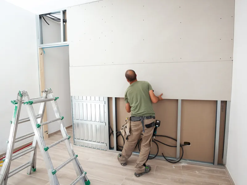 A worker boarding out a wall with a stepladder and offcuts beside him