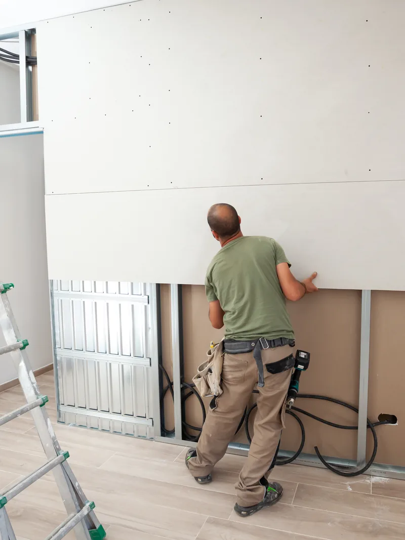 A worker boarding out a wall with a stepladder and offcuts beside him