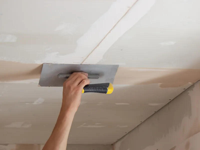 A trowel worked flat across a ceiling overhead