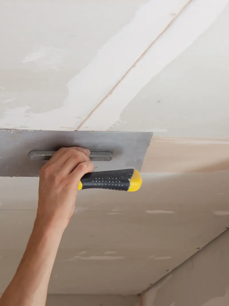 A trowel worked flat across a ceiling overhead
